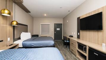 Et hotelværelse med to senge, et skrivebord, en stol, et fjernsyn og en minibar.