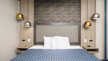 A modern hotel room with a large bed, two bedside tables, a headboard, and pendant lights.