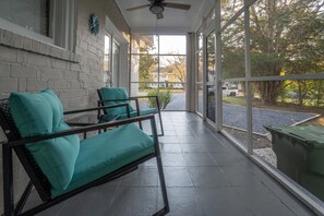 Relax on the covered porch with a view of the surrounding landscape, featuring two cushioned chairs and a ceiling fan.