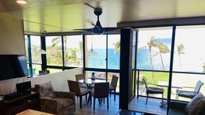 A spacious living area with a large window overlooking the ocean, furnished with a sofa, chairs, and a coffee table. - 406 - Oceanfront One Bed Unit with great views! (Kihei)