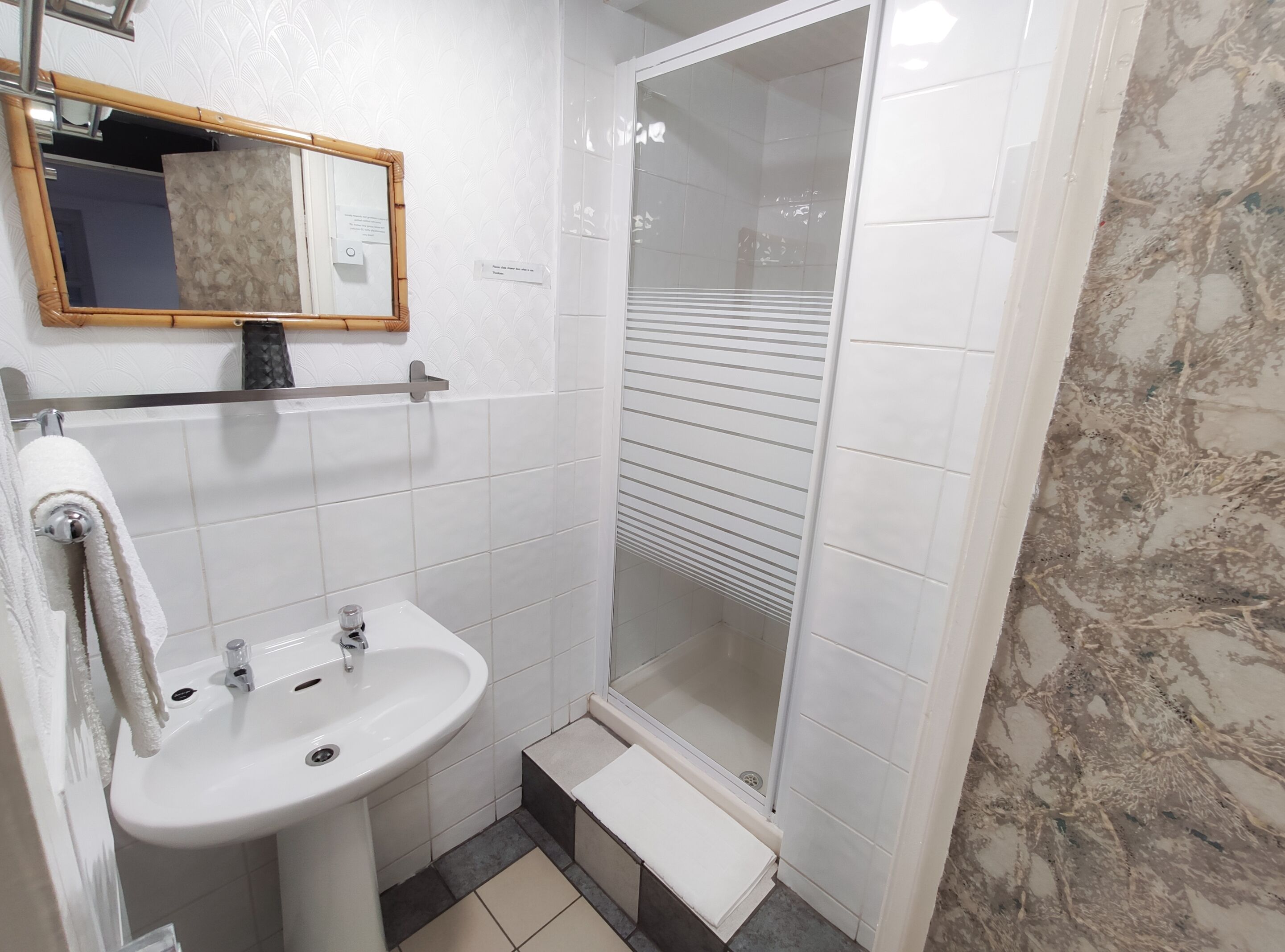 Une salle de bain avec un lavabo blanc, un miroir et une douche.