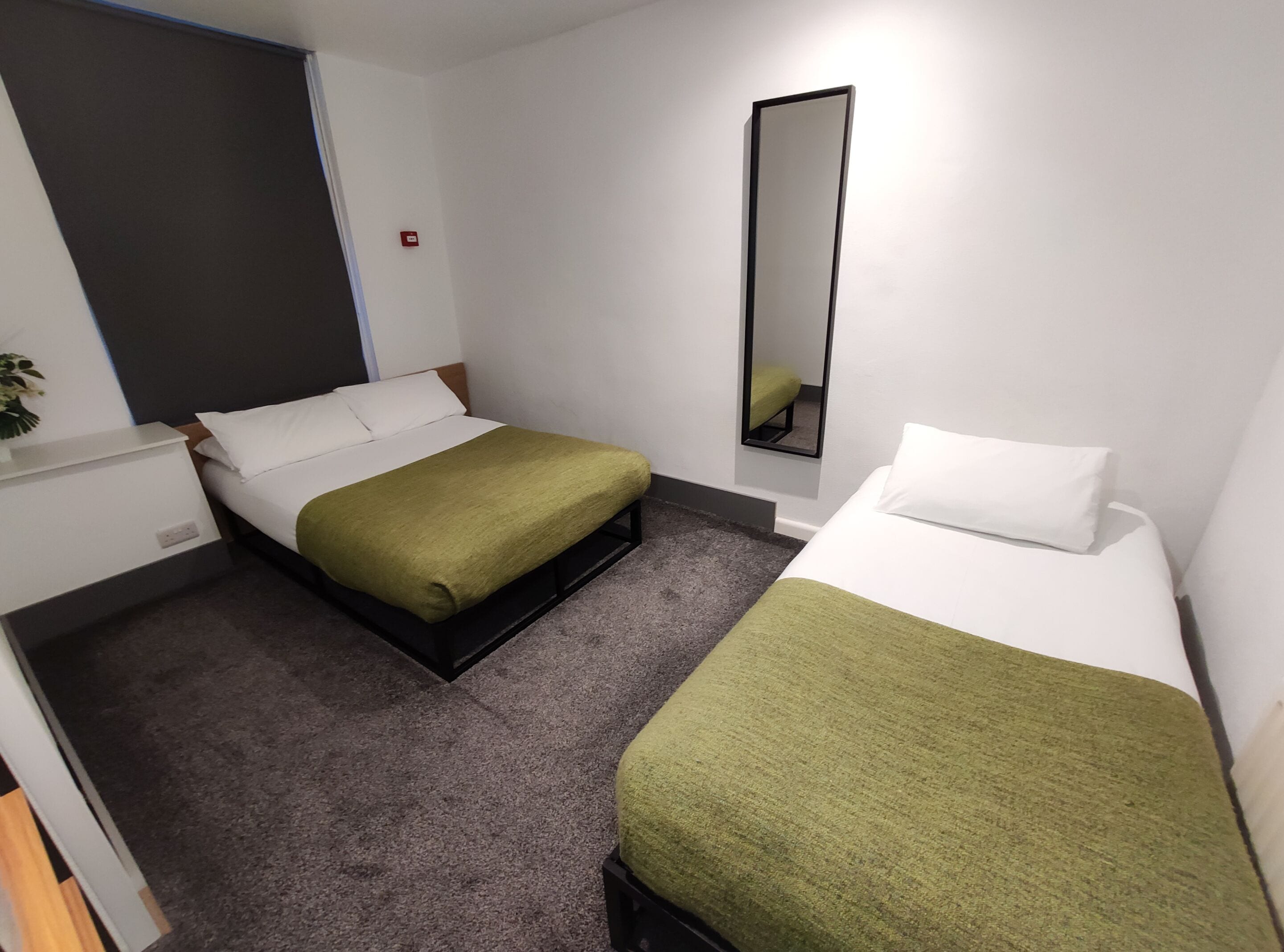 A hotel room with two beds, a small desk, a mirror, and a grey carpet.