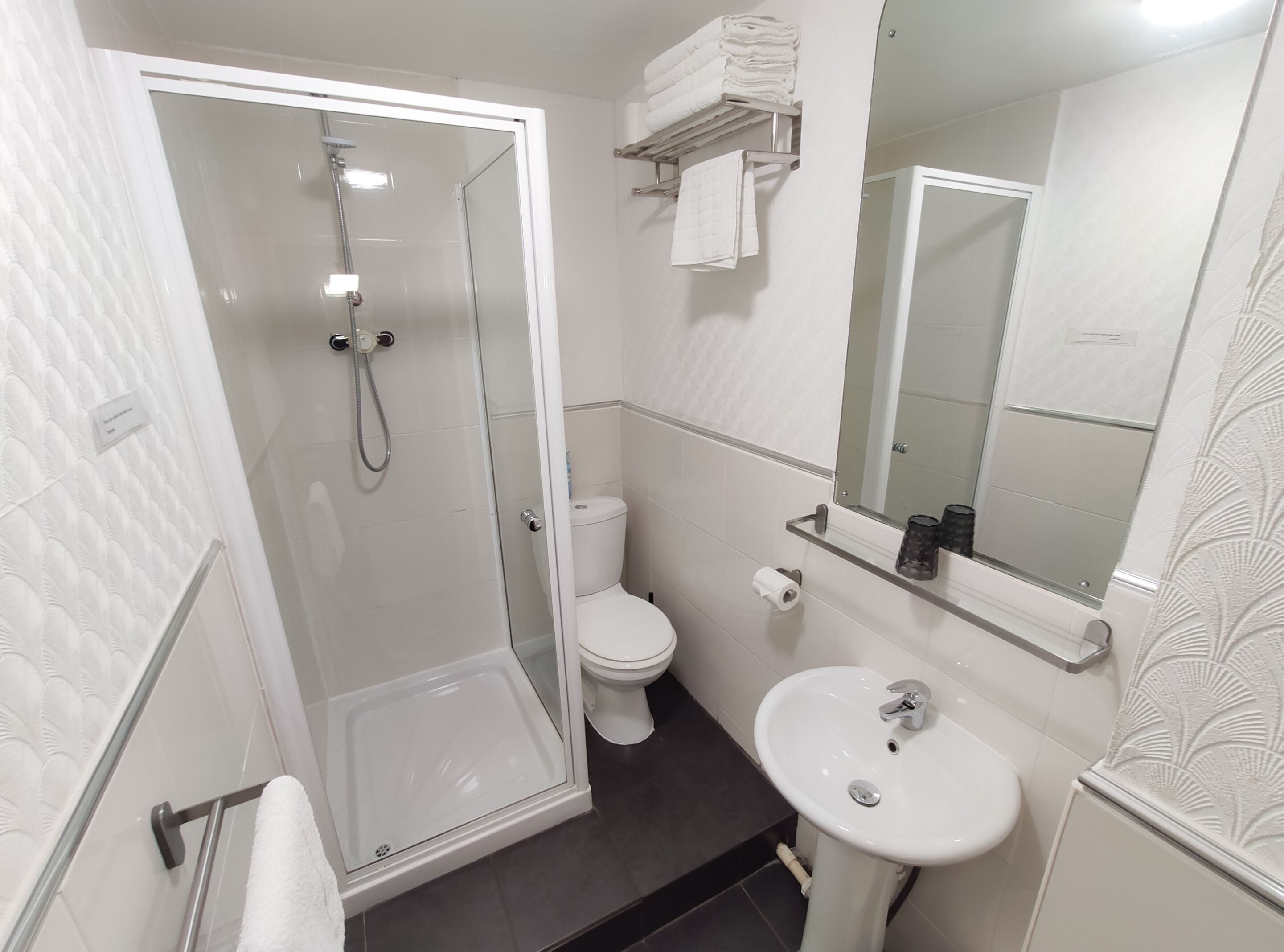 A modern bathroom with a glass-enclosed shower, a white toilet, and a pedestal sink.