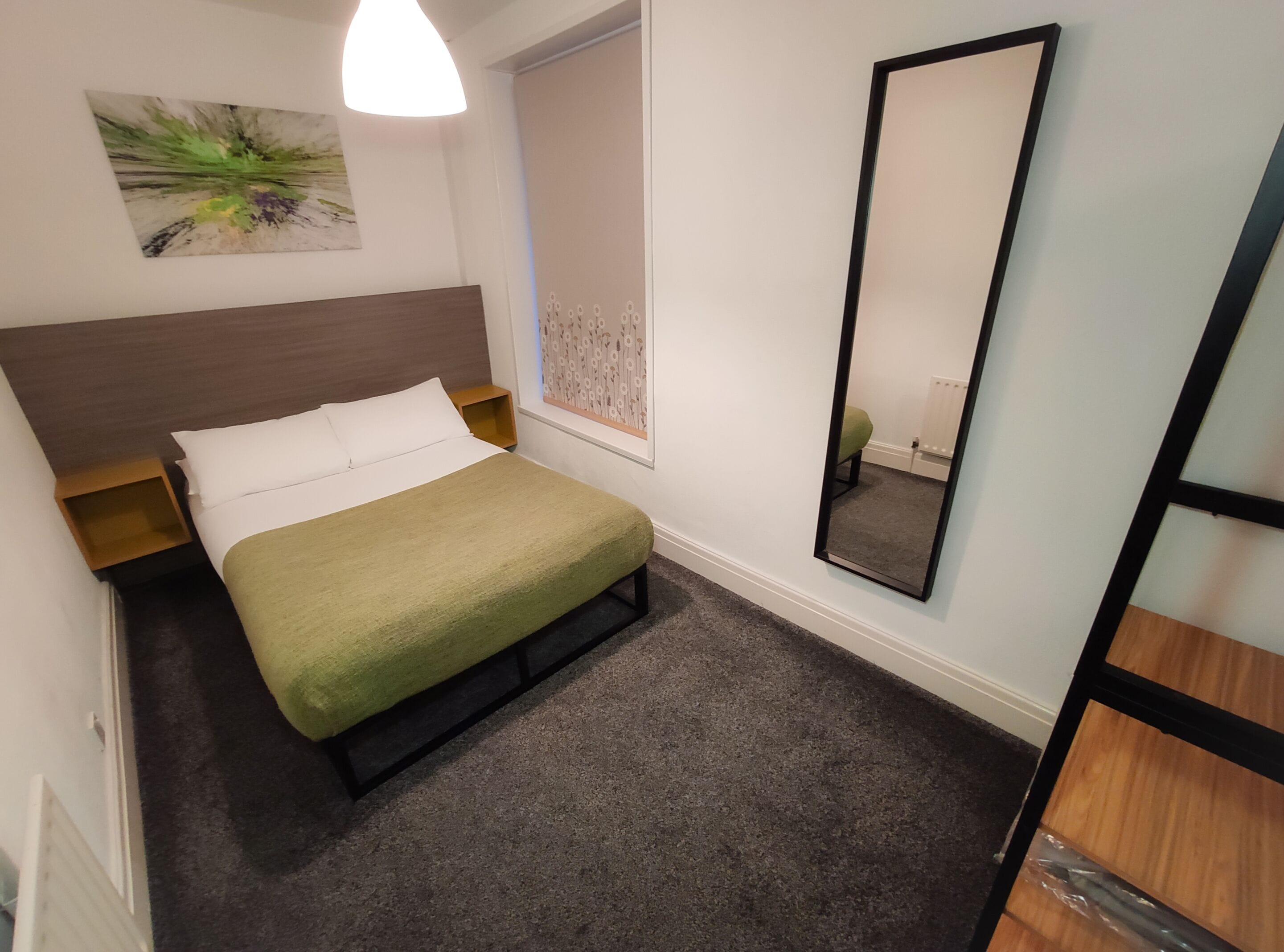 Una camera da letto ordinata con un letto, un comodino, uno specchio e un'opera d'arte appesa al muro.