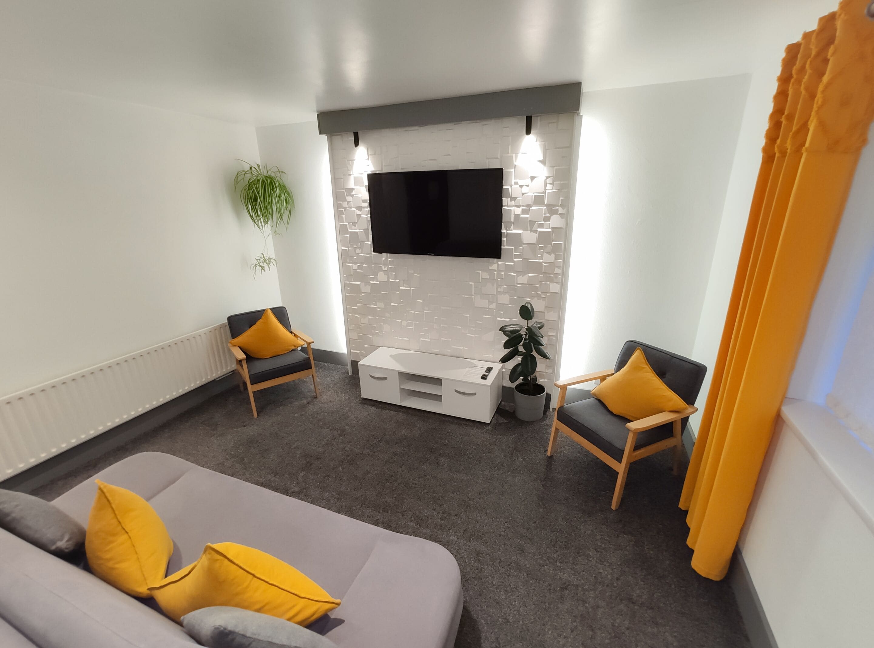 Una sala moderna con un sofá gris, dos sillones, un mueble blanco para el equipo de entretenimiento y un televisor de pantalla plana montado en una pared con textura.