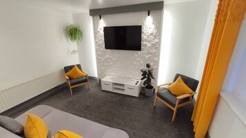 Una sala moderna con un sofá gris, dos sillones, un mueble blanco para el equipo de entretenimiento y un televisor de pantalla plana montado en una pared con textura.
