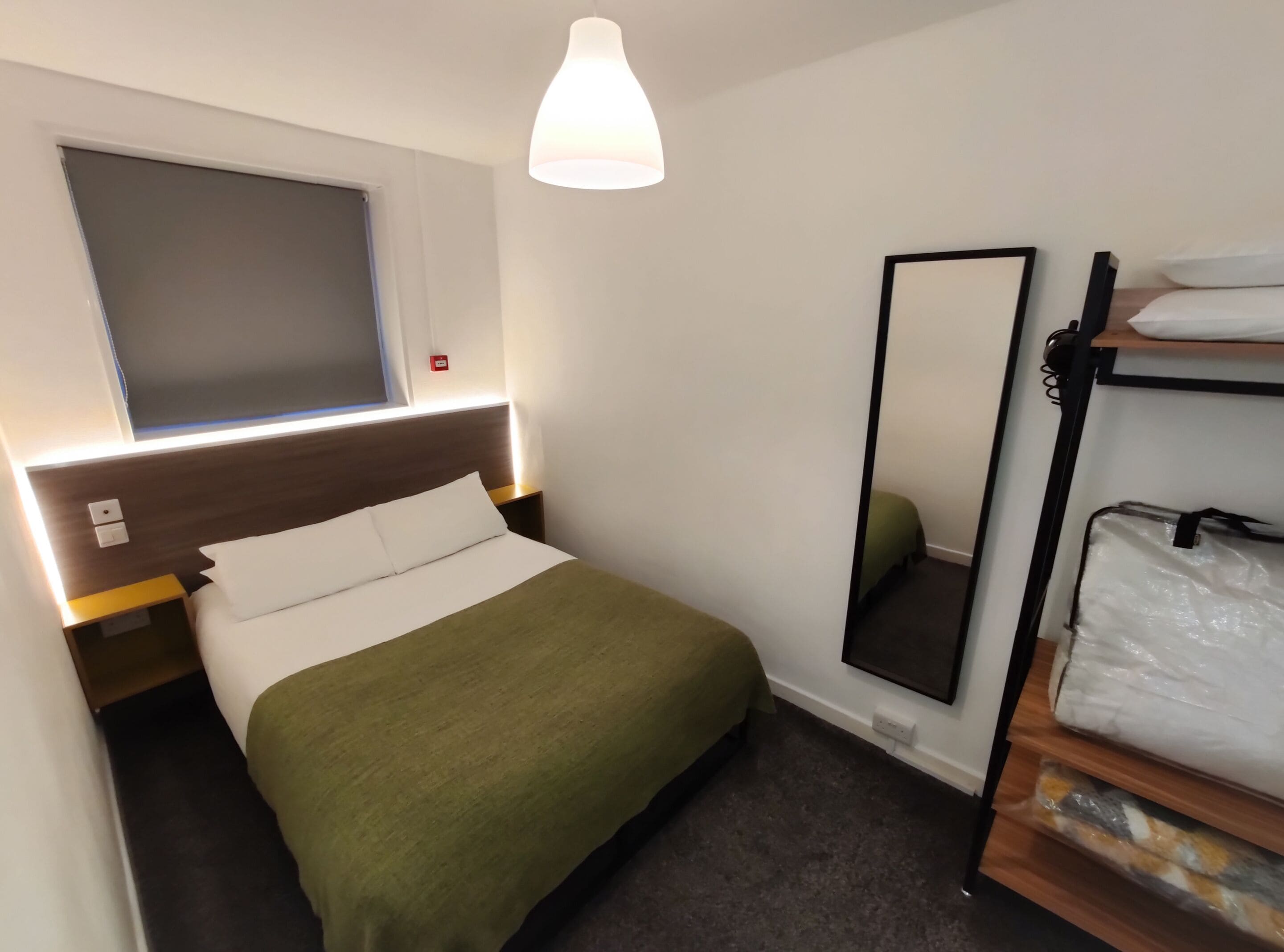 Una habitación de hotel con cama, mesita de noche, espejo y ventana.