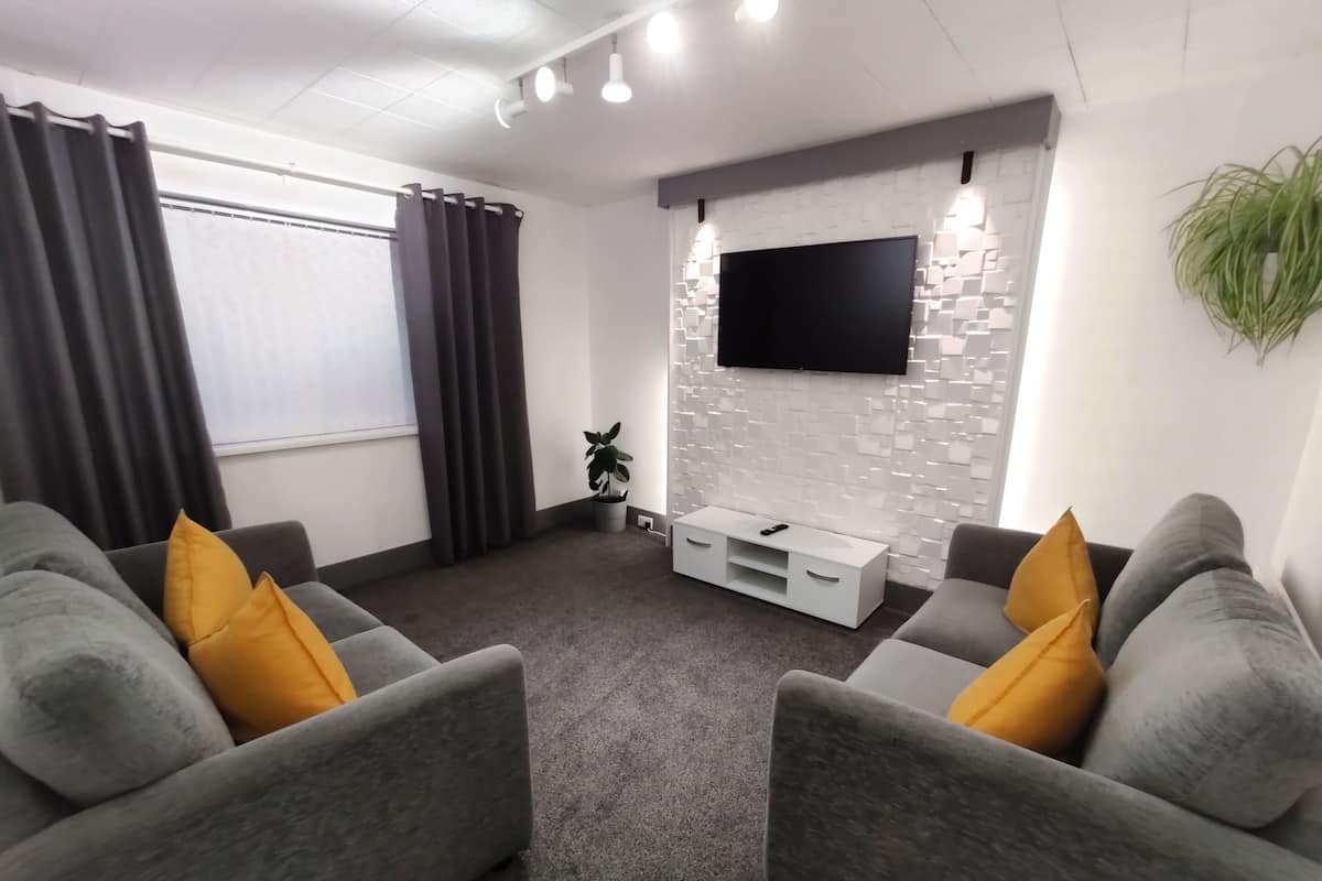 A modern living room with grey sofas, a flat-screen TV mounted on a white brick wall, and a small white cabinet.