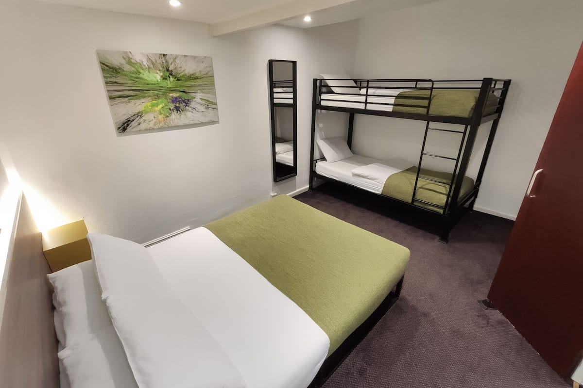 A room with bunk beds, a single bed, a painting on the wall, and a door.