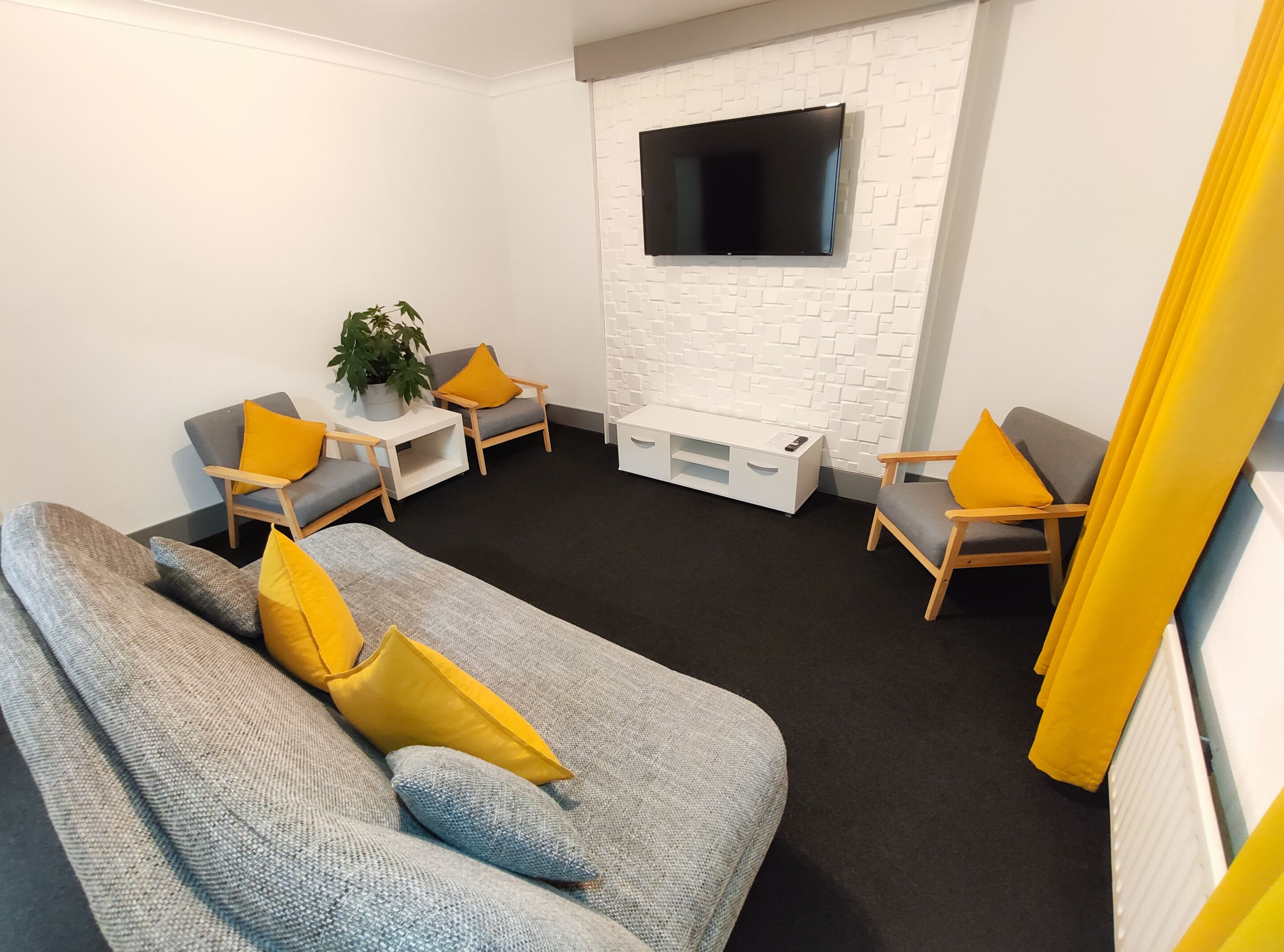 A modern living room with a grey sofa, two armchairs, a white entertainment unit, and a flat-screen TV mounted on a white brick wall.