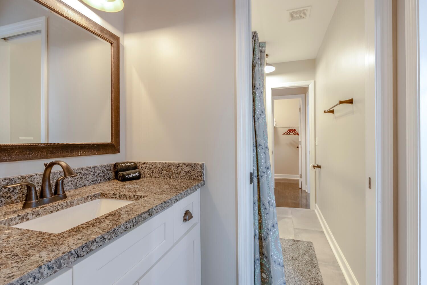 A bathroom with a granite countertop, a sink, a mirror, and a towel holder with 'Makeup' towels.