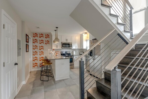 A modern kitchen with white cabinets, a central island, and a stainless steel staircase.