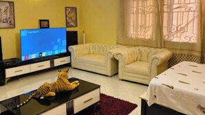 Ein Wohnzimmer mit Flachbildfernseher, einer Couch, einem Couchtisch mit einer Tigerfigur und einem gemusterten Vorhang.