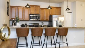 A modern kitchen with wooden cabinets, stainless steel appliances, and three bar stools. - 4873- Great Family Home near Disney, private pool, Storey Lake (Pet Friendly) (Kissimmee)