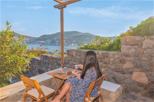 A woman sitting at a table with a view of a coastal town and hills in the background.