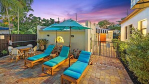 A patio with lounge chairs and a table, surrounded by a brick pathway and greenery. - Great Amenities, Great Location, Amazing Studio! (West Palm Beach)