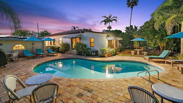 A swimming pool with lounge chairs and umbrellas, surrounded by palm trees and a house. - Great Amenities, Great Location, Amazing Studio! (West Palm Beach)