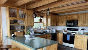 A kitchen with wooden cabinets, a central island, bar stools, a microwave, a stove, and various kitchen appliances.