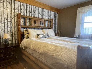 A bedroom with a bed, a nightstand, a lamp, and a wall with a tree and forest design. - Beautiful Cozy Cabin near Historic South Park (Alma)