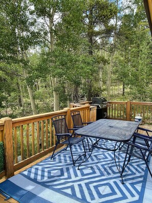 A covered outdoor deck with a table and chairs, surrounded by trees. - Beautiful Cozy Cabin near Historic South Park (Alma)