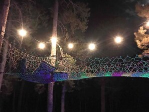 A rope bridge with colorful lights and a netted walkway in a wooded area. - Beautiful Cozy Cabin near Historic South Park (Alma)