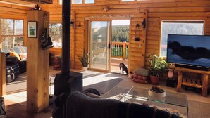 A log cabin interior with a fireplace, a television, and a sliding glass door leading to a deck.