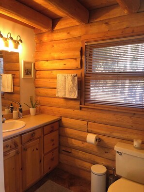 A wooden cabin bathroom with a sink, toilet, and window with blinds. - Beautiful Cozy Cabin near Historic South Park (Alma)