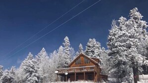 A wooden cabin with a porch, surrounded by snow-covered trees.