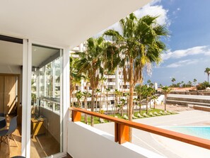 En balkon med udsigt over en pool, palmer og et komplek af bygninger.