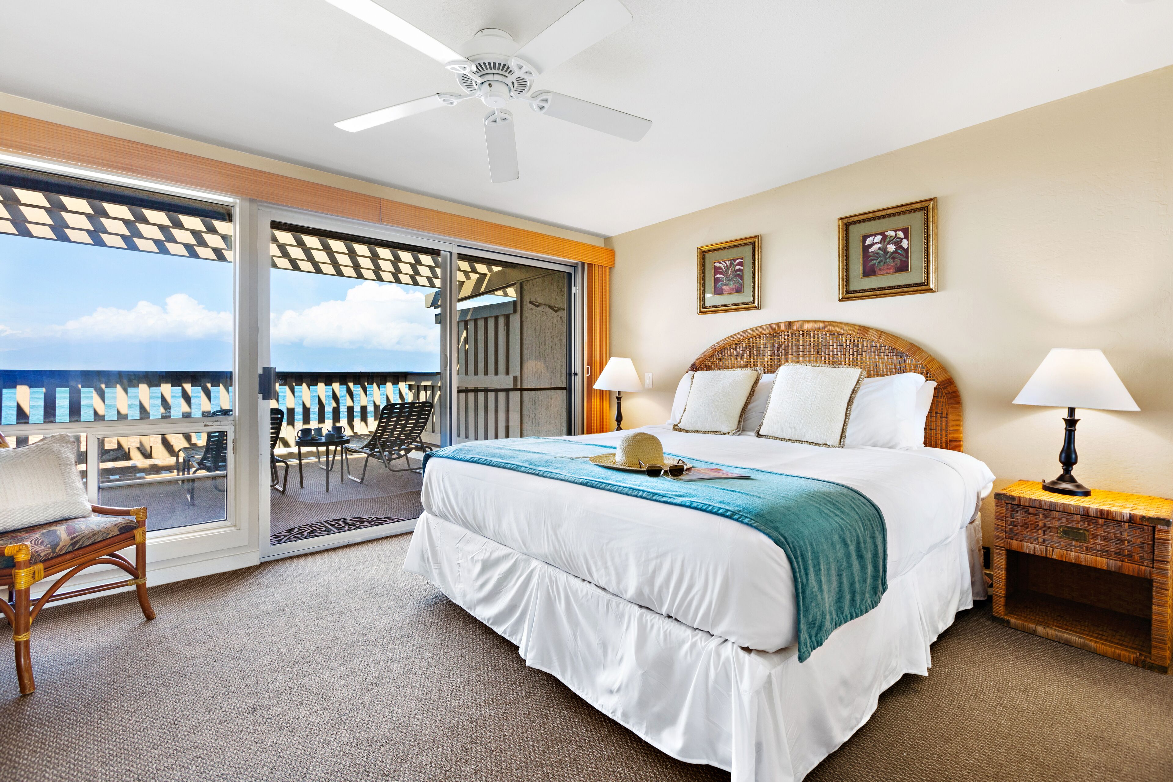A hotel room with a large bed, a ceiling fan, a balcony with a view, and a small table with a lamp.