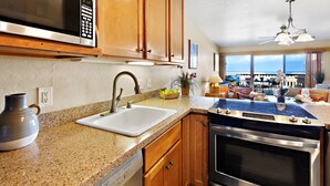 A kitchen with granite countertops, wooden cabinets, a stainless steel microwave, a sink, and an oven. - Double Lanai, Double Ocean Views, all comfort (Lahaina)