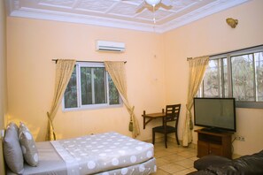 Relax in this cozy space with a comfortable bed, TV, and chair, offering a view of lush greenery.
