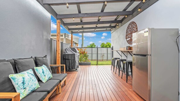 Een overdekt terras met houten terras, een barbecue, een koelkast en een zithoek met kussens.