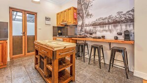 Een keuken met houten kastjes, een centraal eiland met krukken, een groot raam en een muurschildering van een meer.
