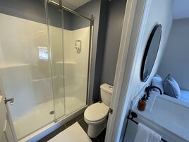 Un baño moderno con ducha de vidrio, inodoro y lavamanos con espejo.