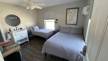 A bedroom with two beds, a desk, a ceiling fan, an air conditioner, a window with blinds, and a map on the wall.