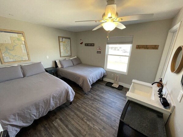 A bedroom with two beds, a ceiling fan, a window, a map on the wall, and a small bathroom with a sink and mirror.