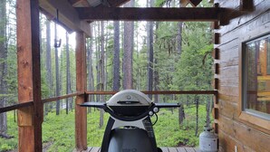 A portable Weber grill on a wooden deck with a view of a forest. - Beyersfort next to Cygnet Lake - Sleeps 5, Private Dock w/ Canoe, No Wi-Fi (Condon)