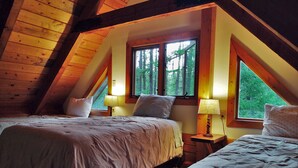 A cozy attic bedroom with two beds, wooden beams, and large windows offering a view of the forest. - Beyersfort next to Cygnet Lake - Sleeps 5, Private Dock w/ Canoe, No Wi-Fi (Condon)
