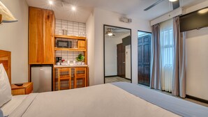 Habitación de hotel compacta con kitchenette, cama, escritorio y puerta corredera a un balcón.