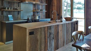 A rustic kitchen with wooden walls, a central island, and a window overlooking greenery.