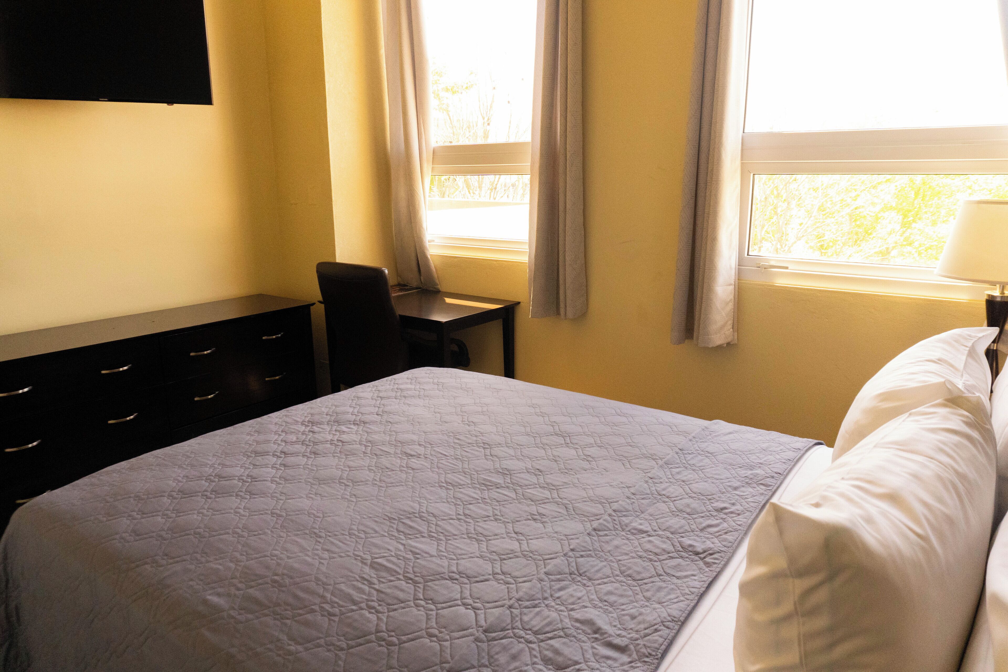 A hotel room with a bed, a desk, a chair, and a TV on the wall.
