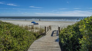 Una passerella di legno che conduce a una spiaggia con un ombrellone blu e lettini.