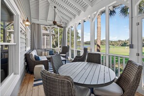 Een overdekt terras met rieten meubilair en een ronde tafel, met uitzicht op een golfbaan.