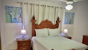 Une chambre à coucher bien rangée, avec un lit en bois, deux tables de chevet avec des lampes, une petite table et deux tableaux accrochés au mur.