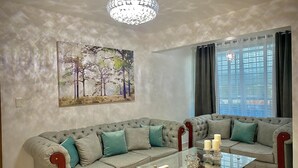 Un salon avec un canapé gris, une table basse en verre et un lustre.