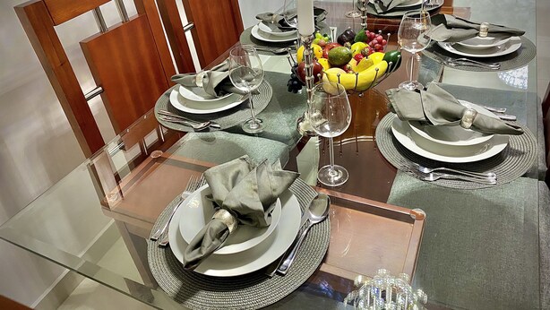 Une table à manger dressée avec des assiettes, des couverts et un panier de fruits.