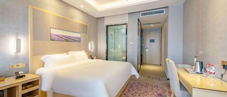 A modern hotel room with a large bed, a desk, and a chair. There is a painting on the wall and a door leading to another room.