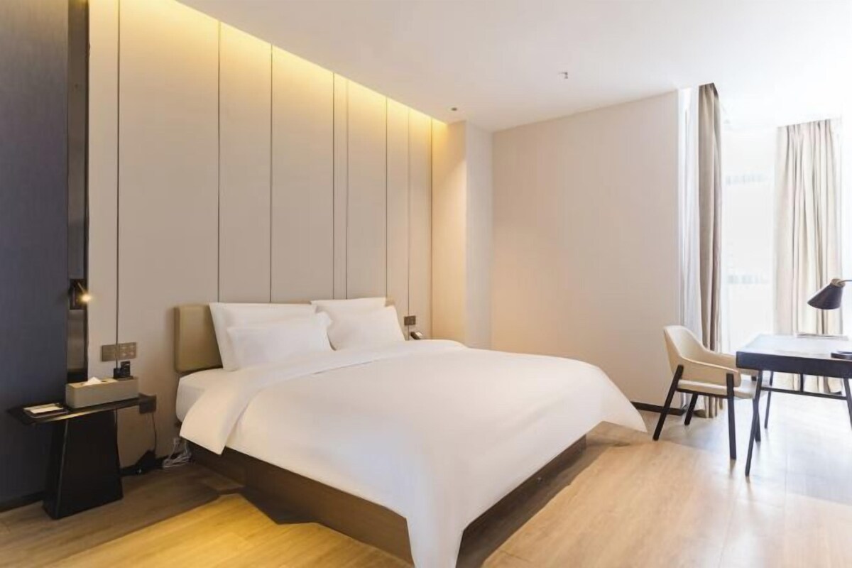 A modern hotel room with a large bed, bedside tables, a desk, and a chair.