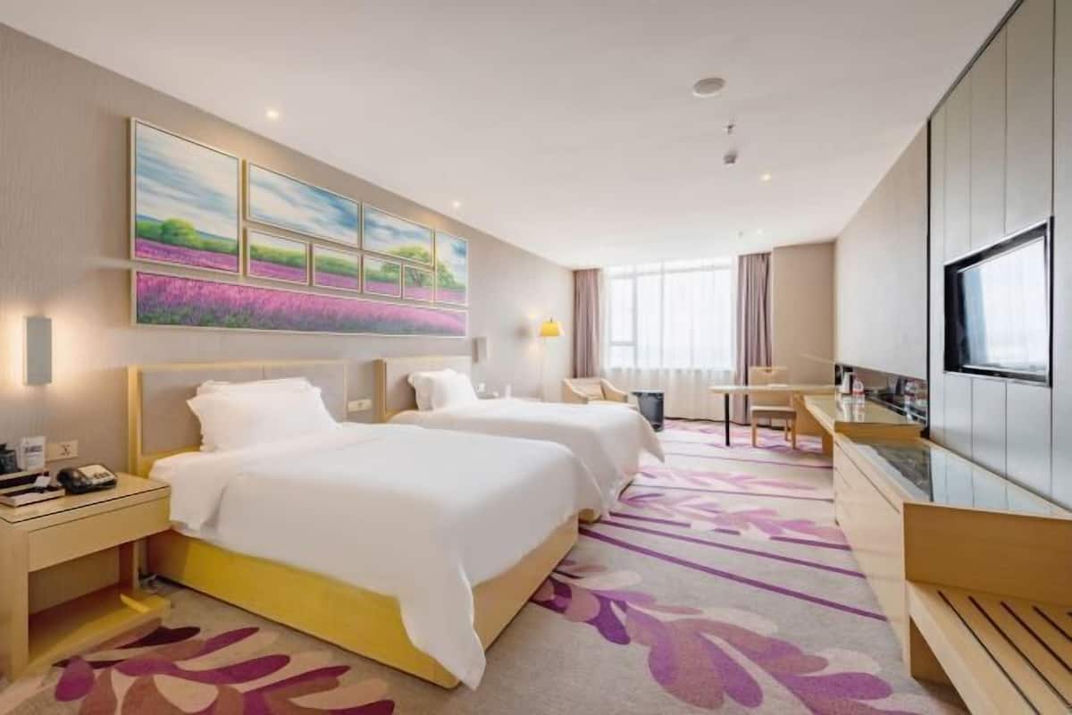 Habitación de hotel con dos camas, un escritorio, un televisor y obras de arte en la pared.